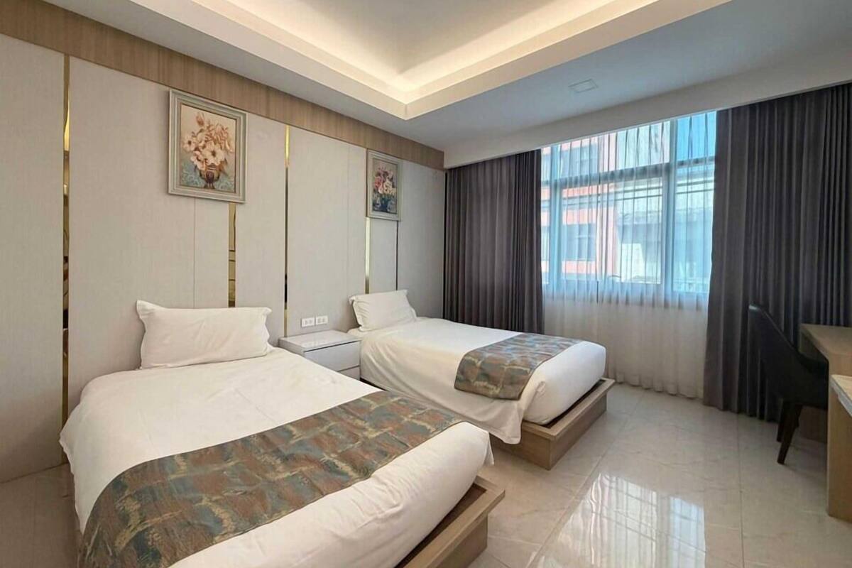 Habitación de hotel con dos camas, un escritorio y un amplio ventanal con cortinas.