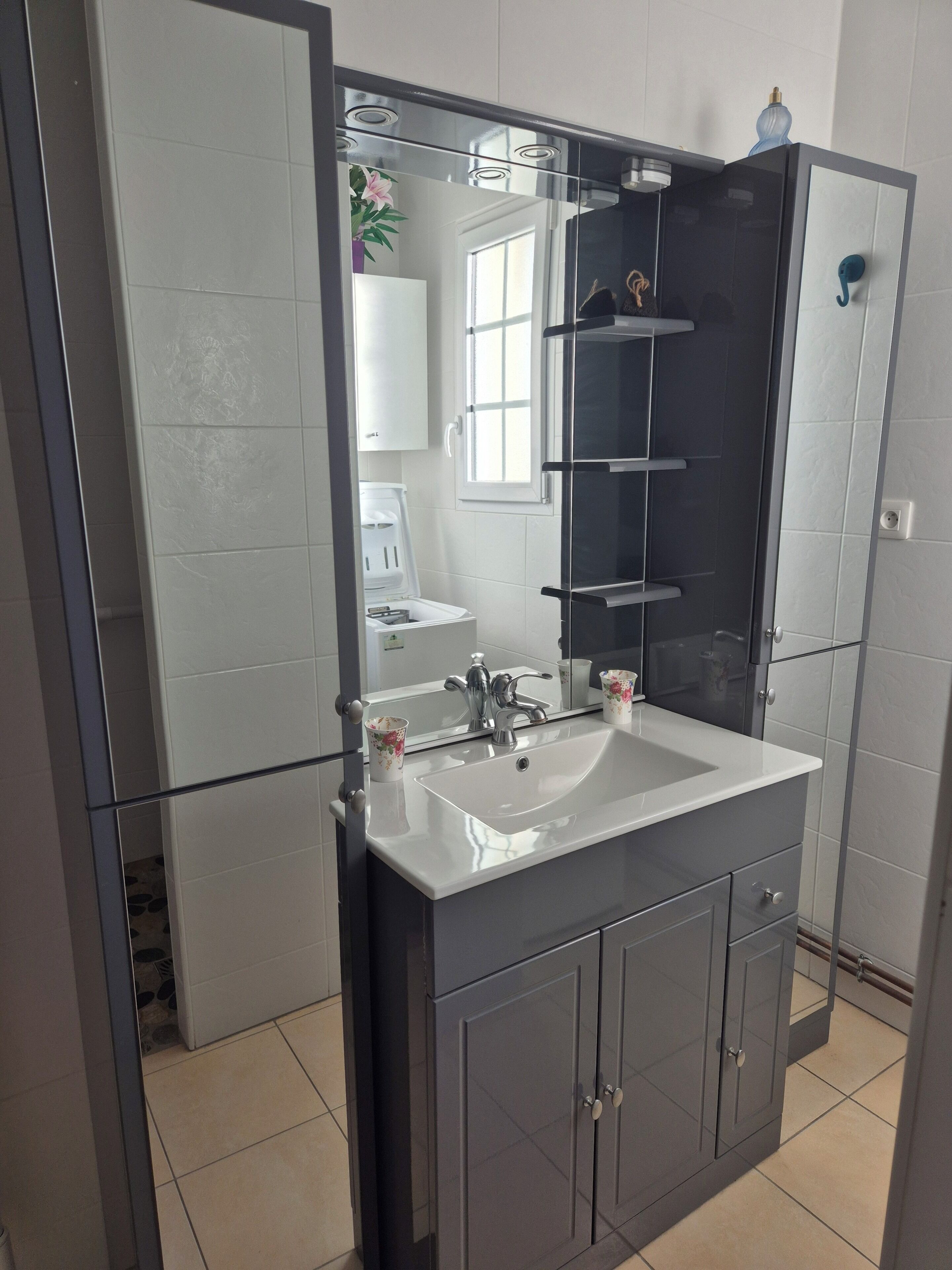 A modern bathroom with a large mirror, a white sink, and grey cabinets.