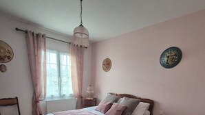 A bedroom with a wooden bed, a bedside table, a chair, and a window with curtains. - The gîte de la muraille welcomes you in the heart of nature, pets not allowed. (Mérignac)