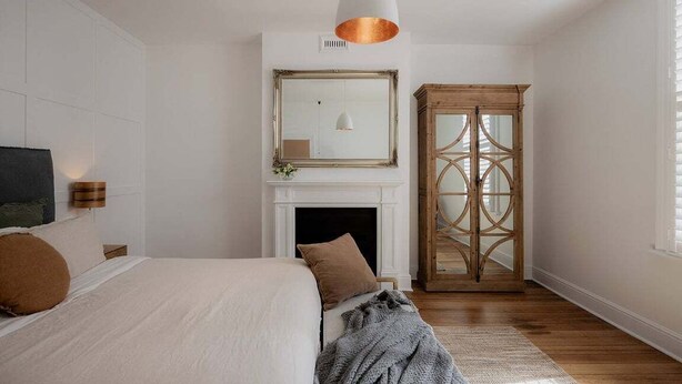 Een slaapkamer met een bed, een open haard, een spiegel en een houten kledingkast.