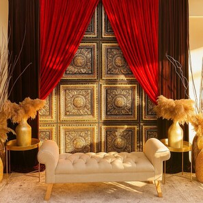 A luxurious room with a tufted sofa, ornate wall paneling, and red curtains.