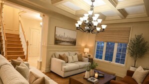 Ein geräumiges Wohnzimmer mit Holzboden, einer Treppe, einer Chandelierleuchtre und einem Stadtbild an der Wand.