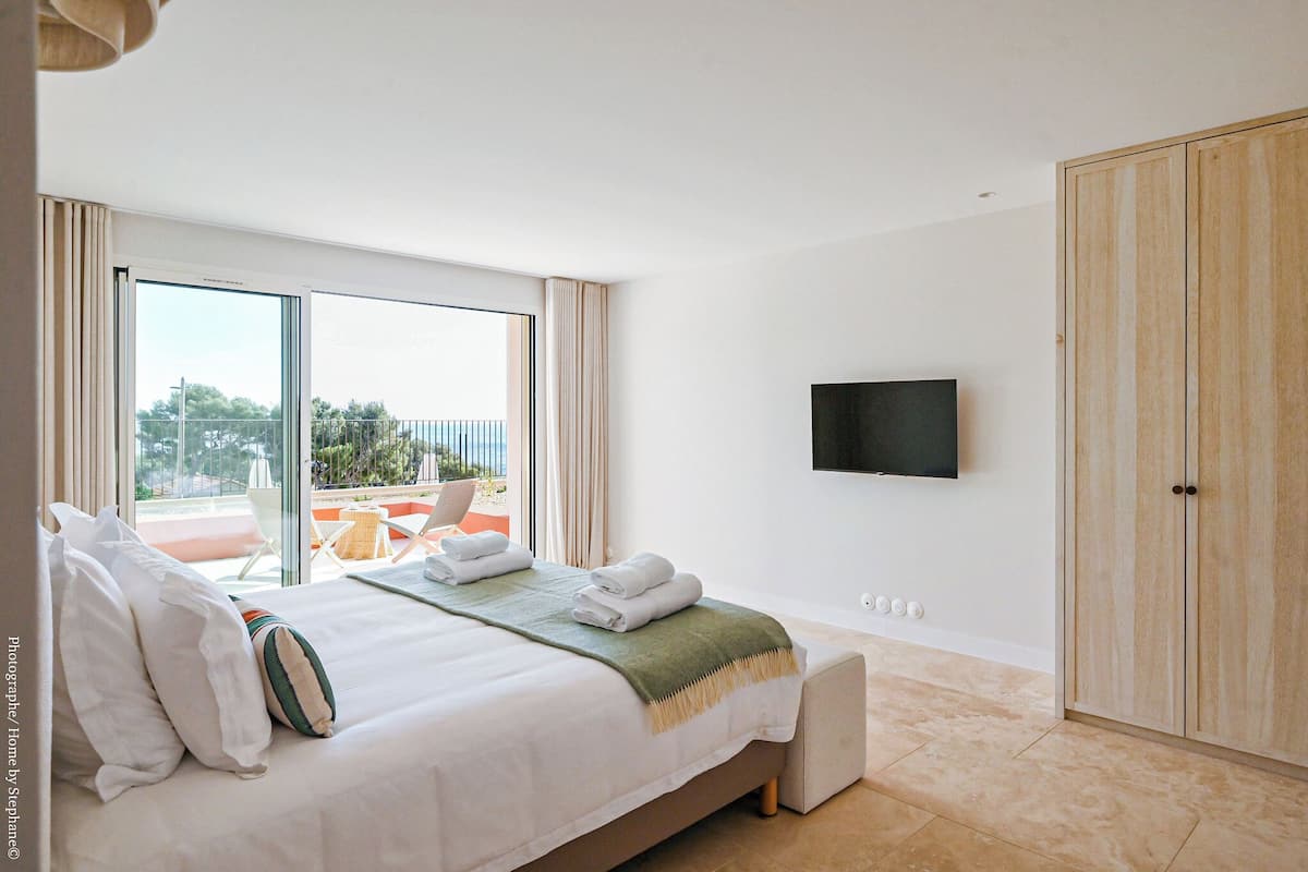 A bedroom with a bed, a TV, a wardrobe, and a balcony with outdoor furniture.