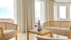En balkon med fletmøbler, et bord med flaske og glas, samt udsigt over byen.