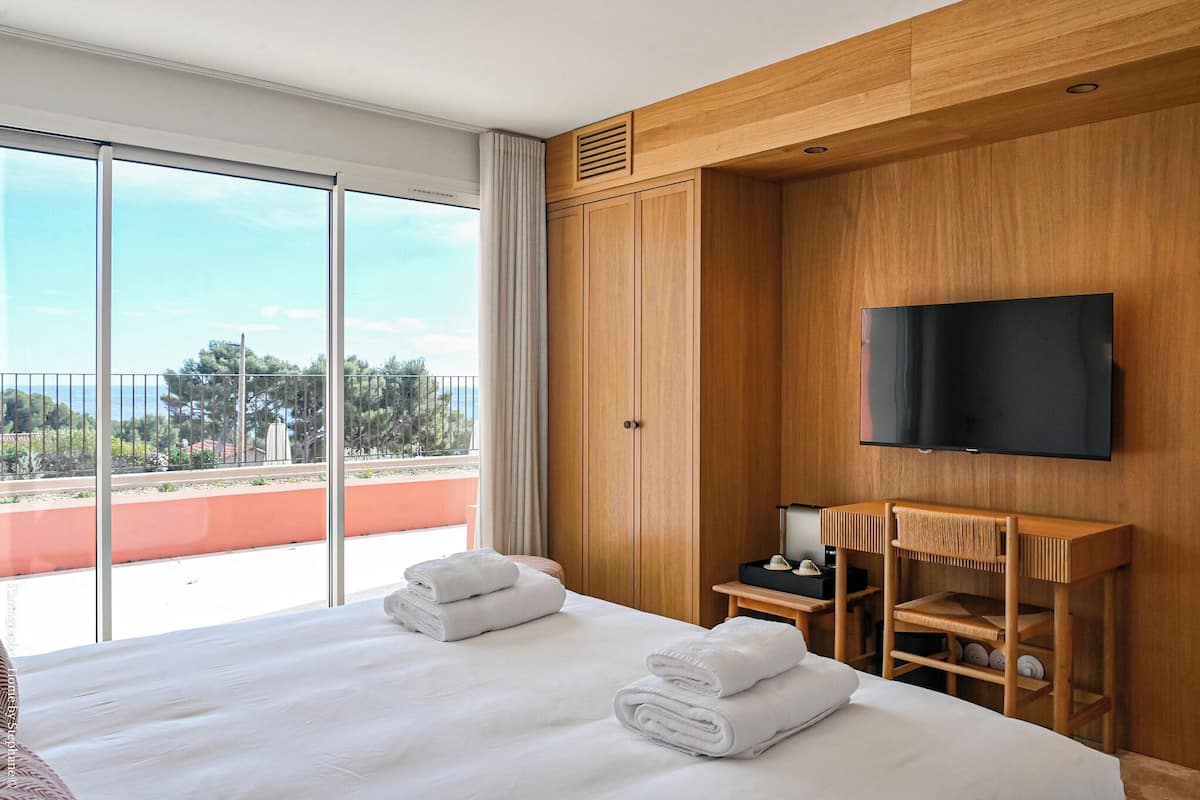 A hotel room with a large bed, a TV mounted on the wall, and a balcony with a view.