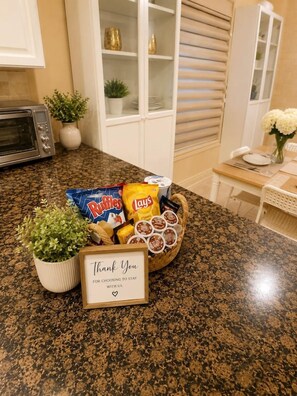 A kitchen counter with a basket of snacks, a potted plant, and a thank you note. - Poolside 4BR by Canterra Stays · Sleeps 12 (Brampton)