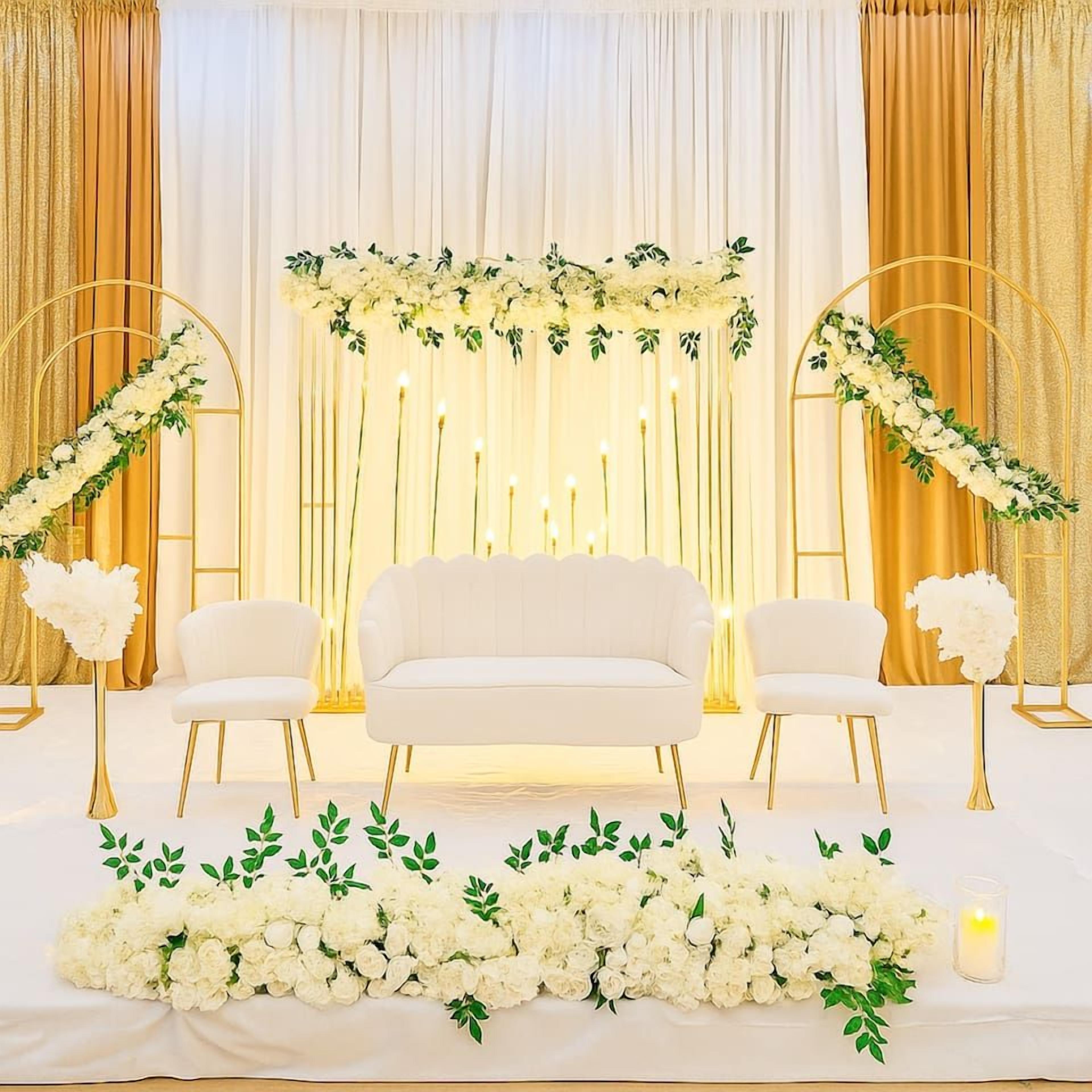 A staged event area with a sofa, chairs, floral arrangements, and candles.