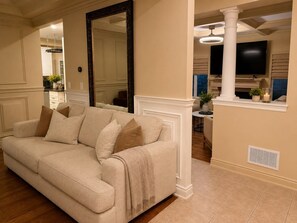 A beige sofa with a throw blanket and pillows, a large mirror, and a television mounted on the wall. - Poolside 4BR by Canterra Stays · Sleeps 12 (Brampton)