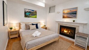 Une chambre à coucher avec un lit, des tables de chevet, une cheminée et deux tableaux accrochés aux murs.