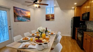 Un coin repas avec une table mise pour le petit-déjeuner, comprenant des croissants, des fruits et du café. La cuisine est équipée de meubles en bois et d’un réfrigérateur.