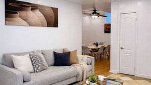 Un salon moderne avec un canapé gris, une table basse en verre et un grand tableau abstrait accroché au mur.
