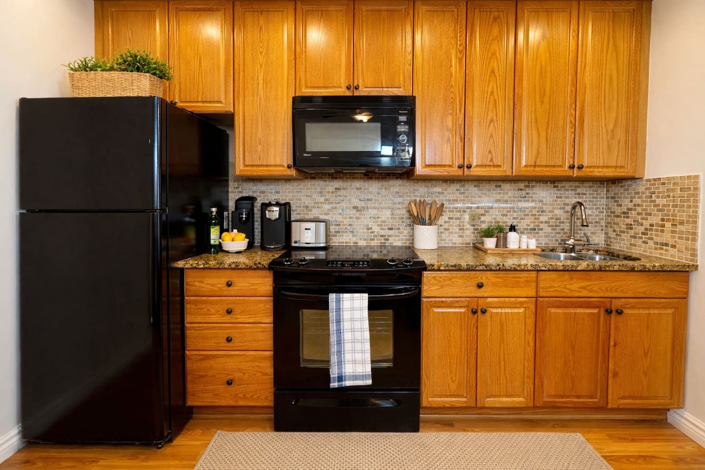 A kitchen with wooden cabinets, a black refrigerator, a microwave, a stove, and a sink.