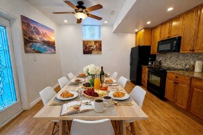 A dining area with a wooden table set for breakfast, a ceiling fan, and wooden cabinets in the adjacent kitchen. - 4BR · 2 Suites by Canterra Stays · Sleeps 8 (Brampton)