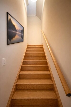 A wooden staircase with a handrail, a wall-mounted picture, and a light fixture at the top. - 4BR · 2 Suites by Canterra Stays · Sleeps 8 (Brampton)