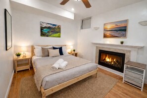 A bedroom with a bed, bedside tables, a fireplace, and two wall-mounted paintings. - 4BR · 2 Suites by Canterra Stays · Sleeps 8 (Brampton)