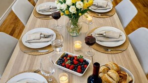 A dining table set for six with white plates, folded napkins, and a vase of yellow and white flowers. - Two Independent Suites · Two Entrances · Sleeps 8 · Fireplace + Sun-Filled Upper Unit (Brampton)