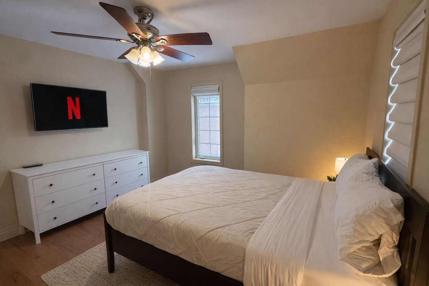 Ein Schlafzimmer mit einem Bett, einem Deckenventilator, einem an der Wand montierten Fernseher und einem Fenster.