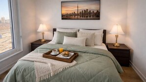 Une chambre d’hôtel avec un lit, deux lampes de chevet, un plateau avec le petit-déjeuner et un tableau représentant un paysage urbain accroché au mur.