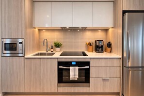 A modern kitchen with stainless steel appliances, a double sink, and wooden cabinetry. - Parking Included · Sauna & Climbing Wall · Steps to Square One · Weekly Stays (Mississauga)