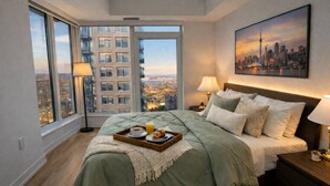 Une chambre d’hôtel avec un grand lit, une vue sur la ville et un plateau de petit-déjeuner posé sur le lit.