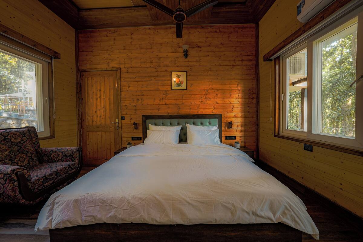 A wooden cabin room with a bed, a chair, and large windows.