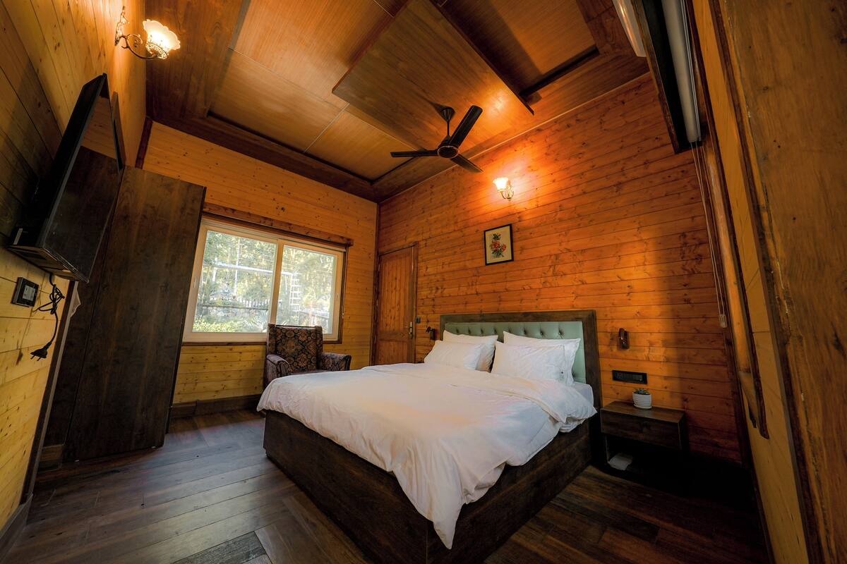 A wooden cabin bedroom with a bed, a ceiling fan, a window, and a nightstand.