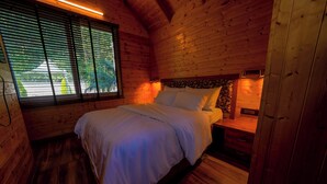 Een houten slaapkamer met een bed, nachtkastjes en een raam met zonwering.