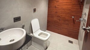 Moderni kylpyhuone, jossa on valkoinen wc-istuin, suuri pesuallas ja puusta tehty korosteseinä.