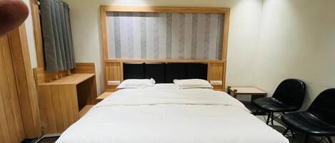 A hotel room with a bed, a wooden headboard, a desk, two chairs, and a window with curtains.