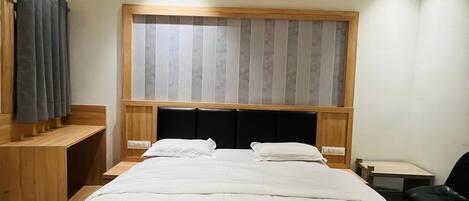 Una cama bien hecha con cabecera de madera, una mesita de noche, una silla y una ventana con persianas.