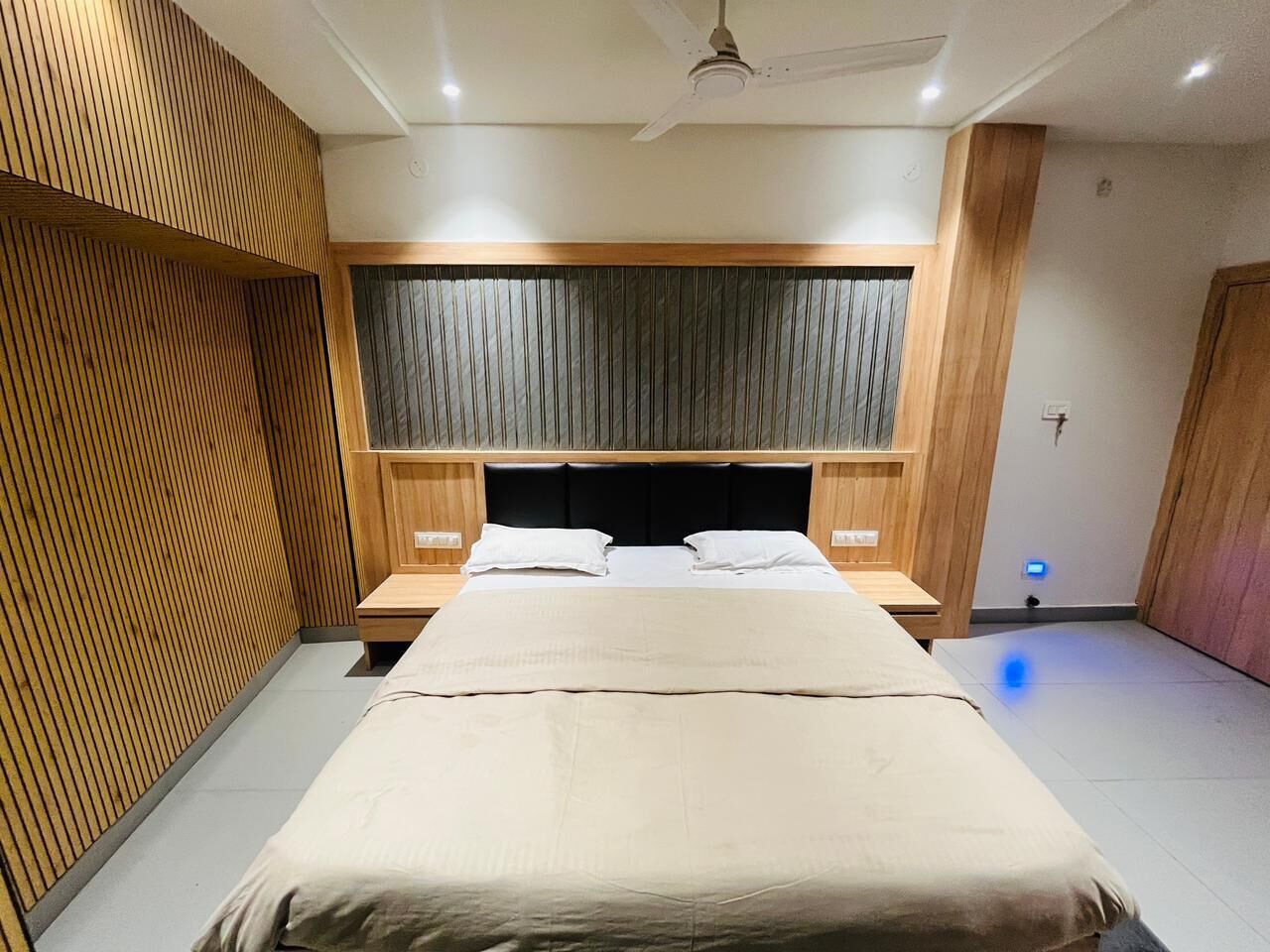Een moderne slaapkamer met een groot bed, houten lambrisering aan de wanden, een plafondventilator en een nachtkastje met een lamp.