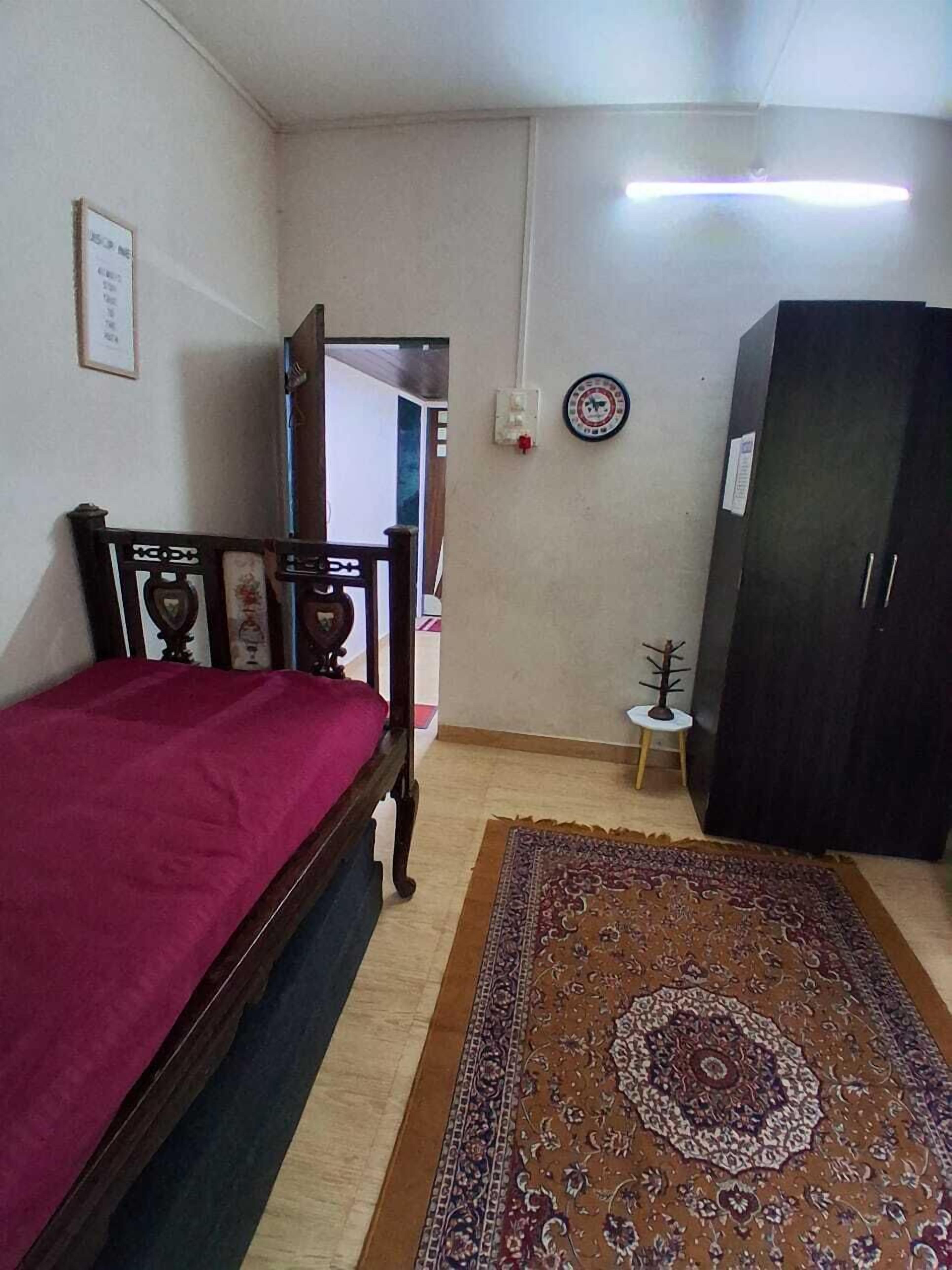 A bedroom with a bed, a wardrobe, a small table, and a rug.