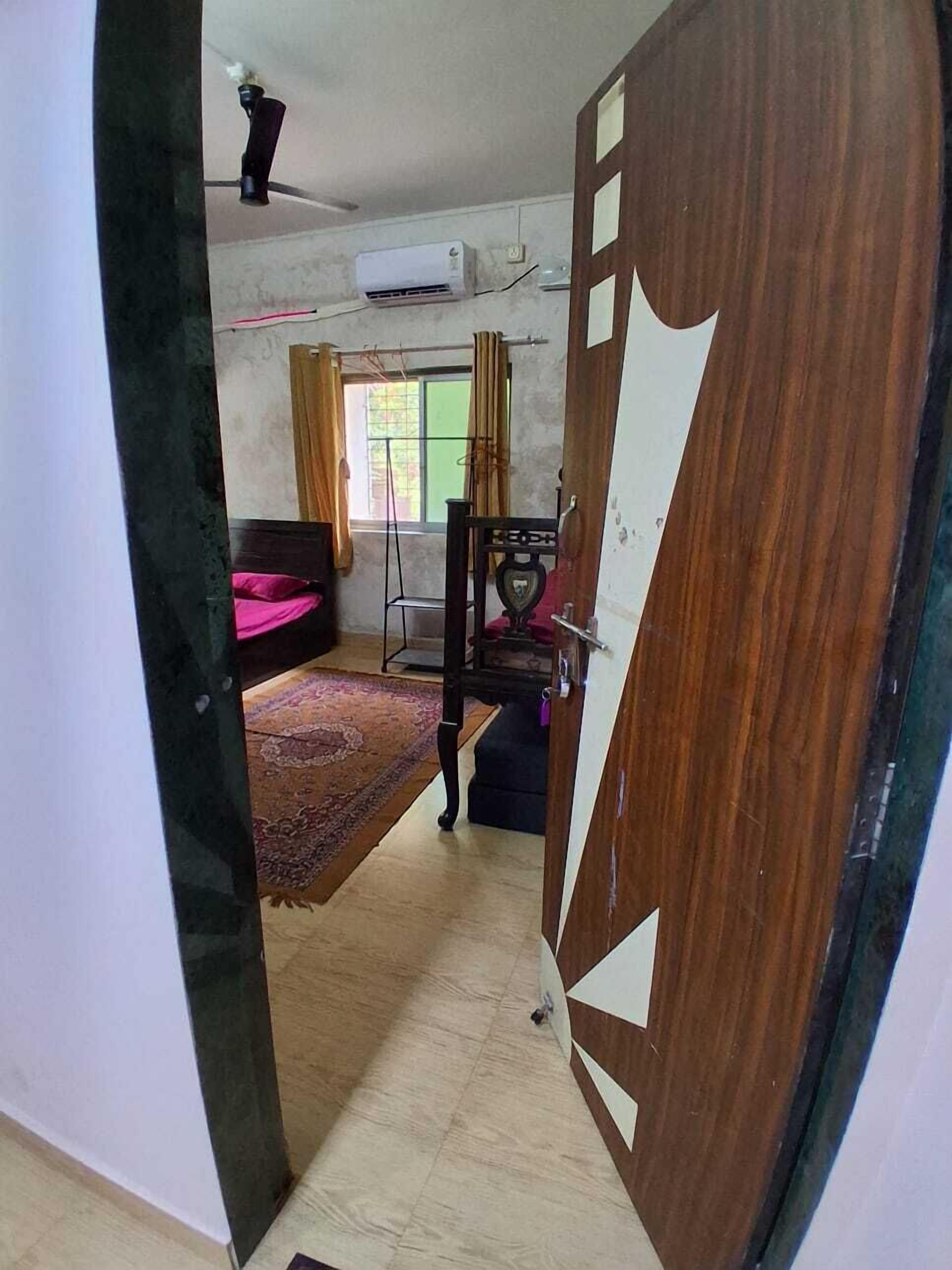 A room with a bed, a desk, a chair, a window with curtains, and an air conditioning unit.
