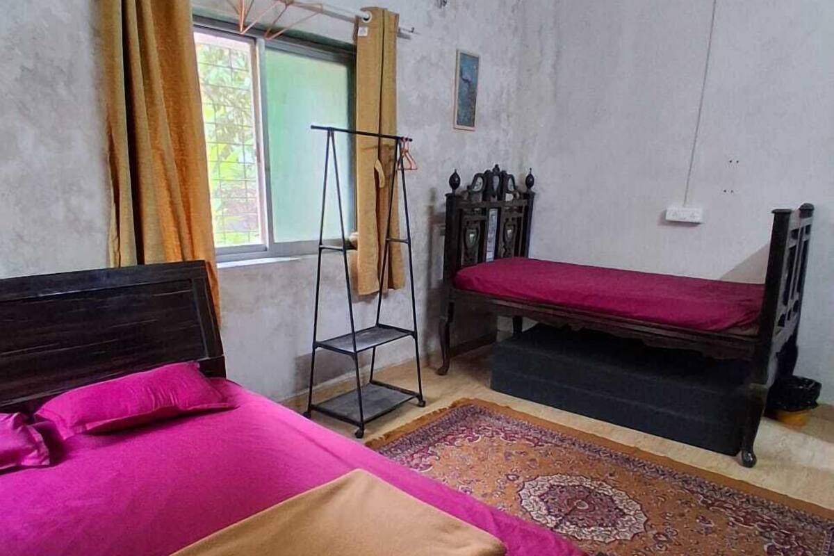 Una habitación con una cama, un pequeño sofá, una estantería y una ventana con cortinas.