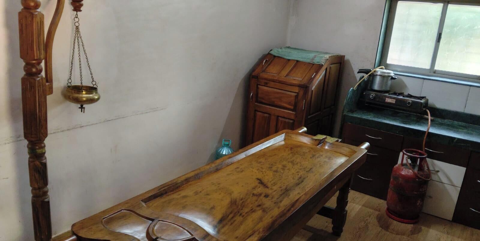 A room with a wooden table, a small cabinet, a gas stove, and a window.
