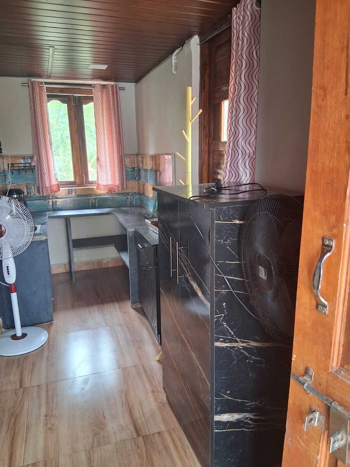 A kitchen with wooden flooring, a marble countertop, a sink, and a window with curtains.