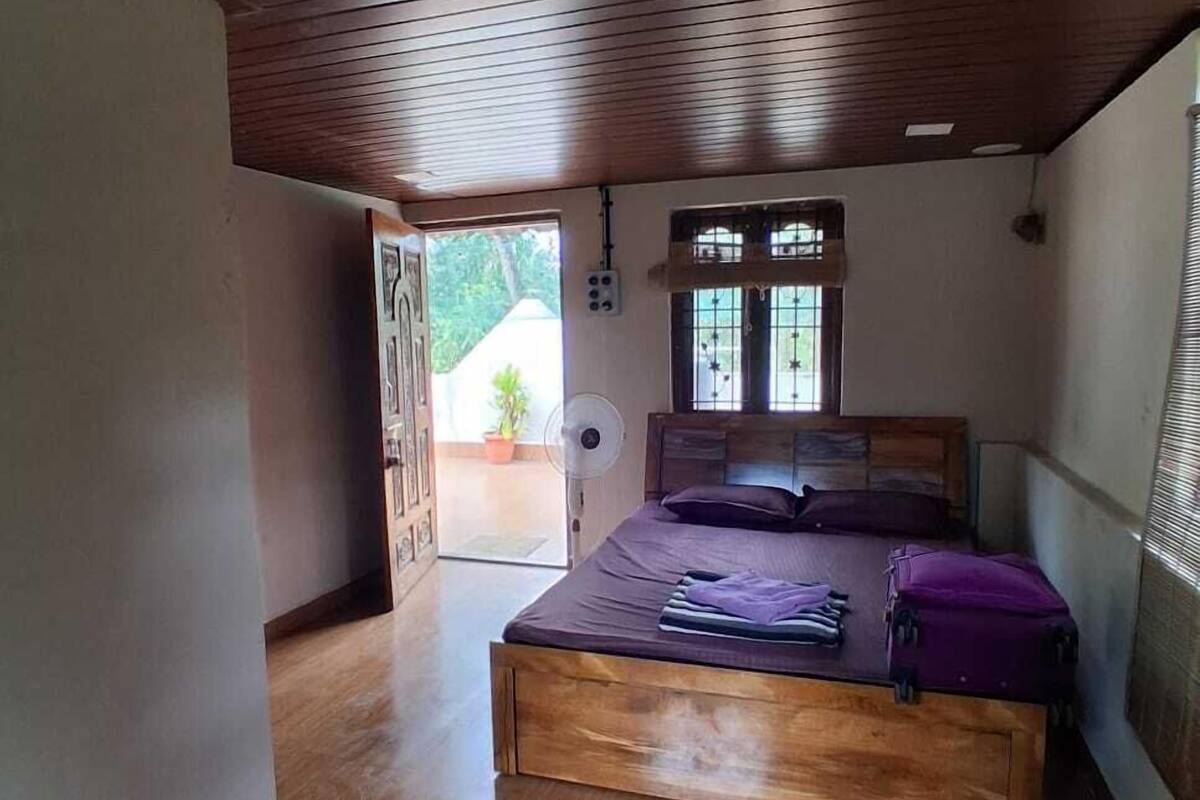 Un dormitorio con techo de madera, una cama, una ventana con rejas y un ventilador.