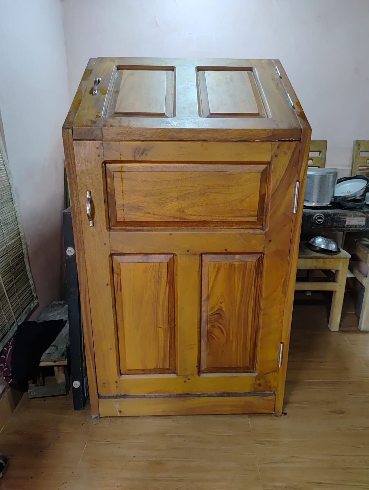 Ein Holzkleiderschrank mit zwei Türen und einer Ablage, in einem Raum mit Holzboden und einem Stuhl im Hintergrund.