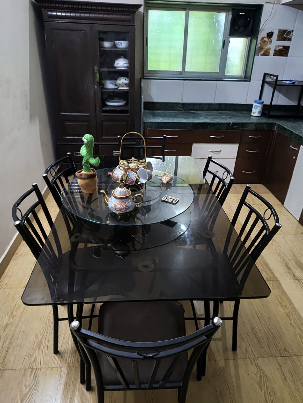 A dining area with a round glass table surrounded by black chairs, a green cactus decoration, and a tea set.