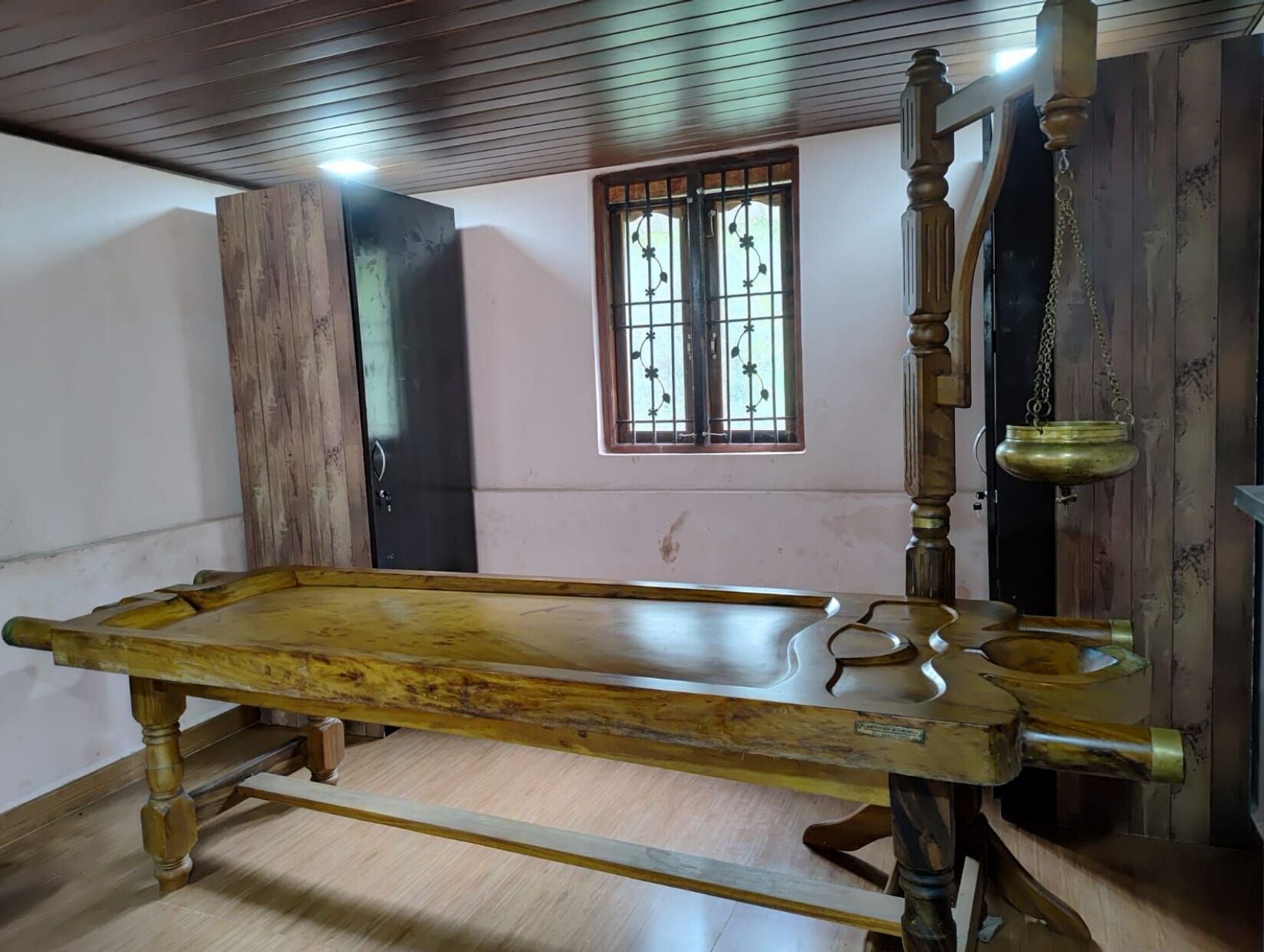A room with a wooden bed, a window with bars, and a wooden door.