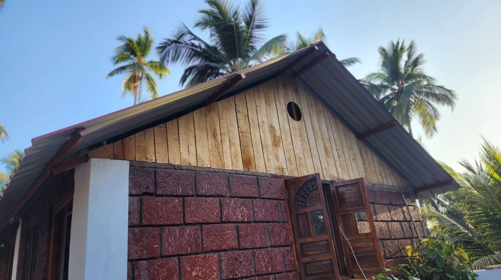 Un bâtiment en bois avec un mur en briques, une porte en bois et un toit en métal.
