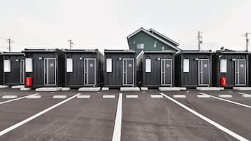 Fila de cabañas portátiles con puertas blancas, numeradas del 31 al 36, en un estacionamiento delimitado por líneas blancas en el suelo.