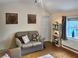 Een gezellige woonkamer met een grijze bank, twee decoratieve kunstwerken, een boekenkast en een raam met gordijnen.