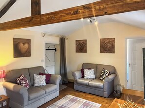 Een knus woongedeelte met twee grijze banken, een houten plafond en drie kunstwerken aan de muur.