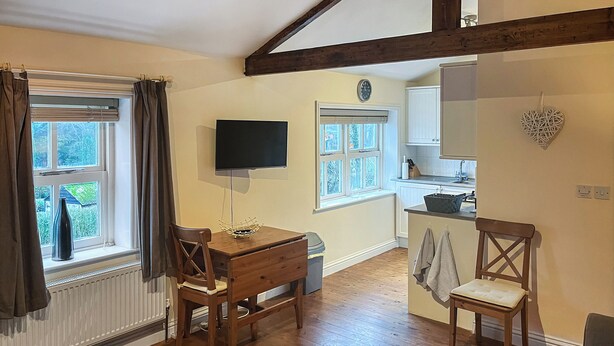 Een gezellige kamer met een houten tafel, twee stoelen, een televisie en een kitchenette met een decoratie in de vorm van een hart.