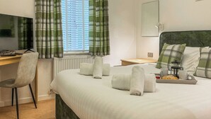 A neatly made bed with rolled towels, a bedside table with a lamp, a chair, and a desk with a computer. - 2 bedroom accommodation in Rock (Rock)