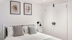 Een net opgemaakt bed met een wit hoofdbord, grijze en witte kussens, een grijze plaid en twee opgerolde handdoeken op het bed.