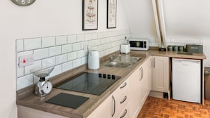 Een moderne keuken met witte kasten, een roestvrijstalen spoelbak, een broodrooster en een magnetron. Er hangen afbeeldingen in lijsten aan de muur en een klok boven de spoelbak.