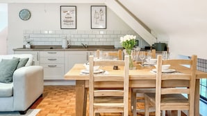 Een moderne keuken met witte kasten, een houten eettafel voor vier personen en een witte bank in de woonkamer.