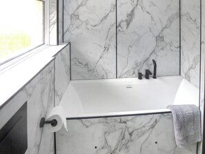A bathroom with a marble wall, a bathtub, and a window. - 3 bedroom accommodation in Whitestone (Whitestone)
